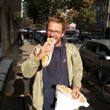 The author of the article smiling and taking a bie from a baguette